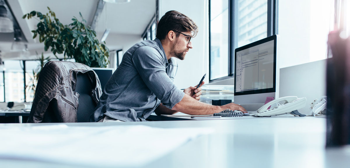 Man at office desk with computer and cell phone planning a DLP strategy