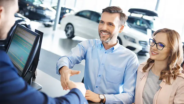 Happy Car Salesman And Clients Shaking Hands