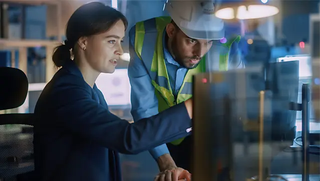 People Looking At Computer Screen At A Manufacturing Plant